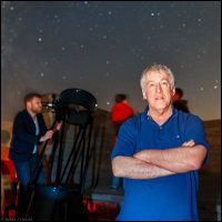 Mike Simmons with a telescope and stargazers in the background looking at the night's sky