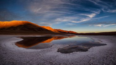 Image shows a saline lake among salty terrain in a desert with a mountain in the background. Taken from somewhere in the Atacama Desert.